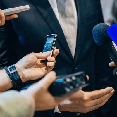 Person being interviewed with multiple microphones and smartphones held by reporters